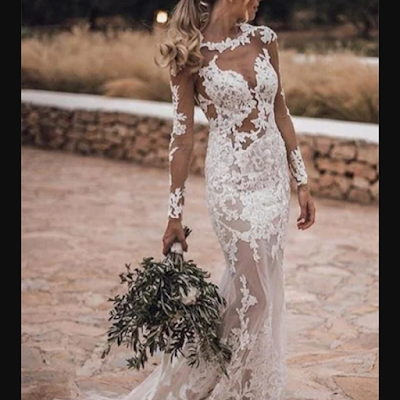 Vestido de noiva rendado com efeito ilusão Noiva a usar vestido de noiva rendado com efeito ilusão, mangas compridas transparentes e silhueta ajustada, num ambiente exterior rústico