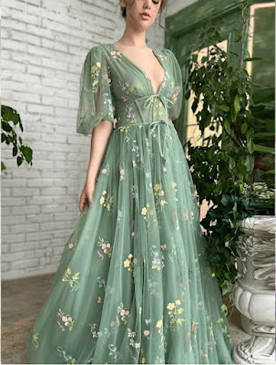 Sage Green Elegance: Ethereal Tulle Gown with Botanical Embroidery A woman wearing a floor-length, sage green tulle dress with a deep V-neckline and puff sleeves. The gown is adorned with delicate colorful floral embroidery, featuring tiny yellow and pink blossoms. The dress has a corset-inspired bodice with ribbon ties, creating an ethereal and fairy-tale aesthetic perfect for a formal garden wedding or a woodland ceremony.