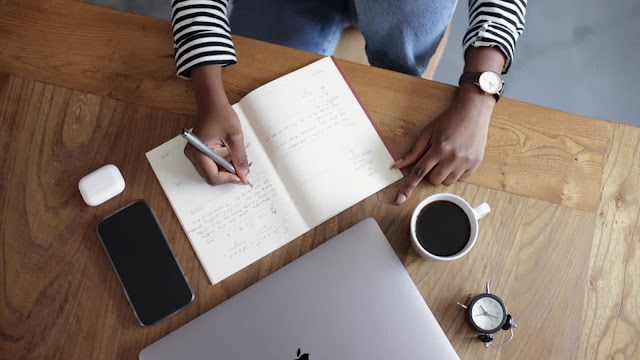 Análise SWOT pessoal: planeamento e reflexão Pessoa a escrever num caderno num ambiente de trabalho, com portátil, café e smartphone, a planear uma análise SWOT pessoal.
