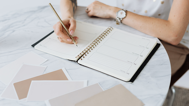 Pessoa a escrever num planner semanal sobre uma mesa de mármore, com amostras de cores ao lado — planeamento e organização pessoal.