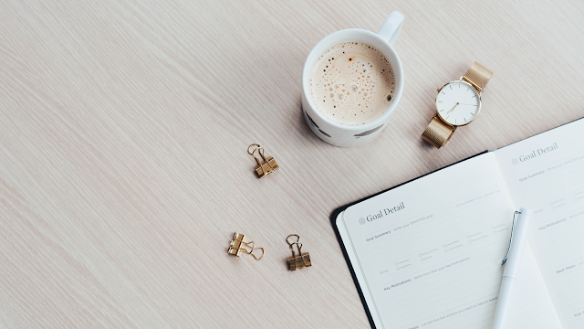 Rotina organizada: café, relógio e agenda Caneca de café, relógio dourado e agenda aberta com espaço para definir objetivos, sobre uma secretária de madeira clara