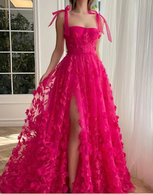 Vibrant Fuchsia statement: 3D Floral Appliqué Gown with Slit A full-length photo of a woman in a dramatic, bright fuchsia pink gown. The dress is strapless with a corset-style bodice and shoulder tie-straps. It is covered in intricate 3D floral appliqués and embroidery. A high slit reveals her leg. The aesthetic is bold, glamorous, and eye-catching.