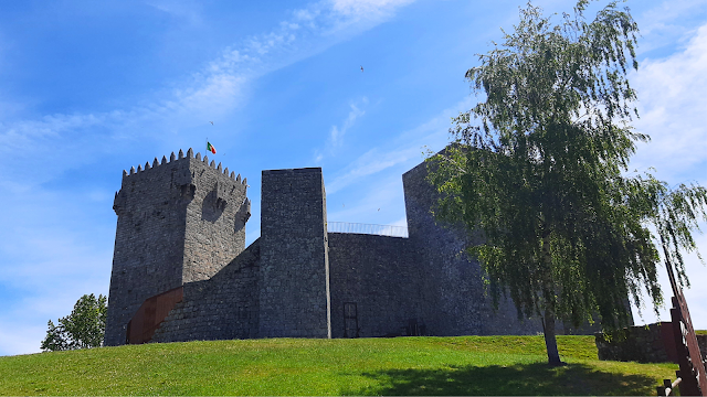 Castelo de Montalegre sob o céu azul de Trás-os-Montes Vista exterior do Castelo de Montalegre, com muralhas em pedra, torre de menagem e árvore em primeiro plano, num dia de céu azul em Trás-os-Montes.