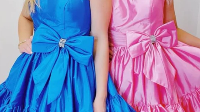 Rhinestone and Bow Satin Party Dresses in Blue and Pink Detailed close-up showing two women standing side-by-side, wearing matching satin cocktail dresses with large statement bows at the waist, cinched by sparkling rhinestone rings. The woman on the left is in a vibrant royal blue dress, and the woman on the right is in a candy pink dress. Both dresses feature voluminous, tiered, and ruffled skirts. Only the dresses, bows, and a hint of the wearer's arms and shoulders are visible against a simple white studio background.