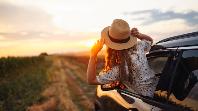 Férias, liberdade e novos começos Mulher com chapéu de palha encostada à janela de um carro, apreciando o pôr do sol durante as férias de verão, simbolizando liberdade e momentos de pausa.