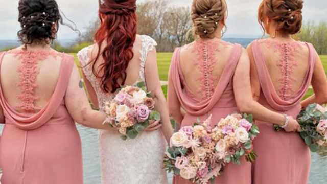 A Elegância da Harmonia: Como Escolher Paletas de Cores para Madrinhas e Convidadas Foto de costas de uma noiva vestida de branco ao lado de três madrinhas vestindo vestidos longos em tom de rosa seco com detalhes em renda e transparência nas costas. Todas seguram buquês florais com tons de rosa, creme e verde, em um cenário externo com gramado e água ao fundo.