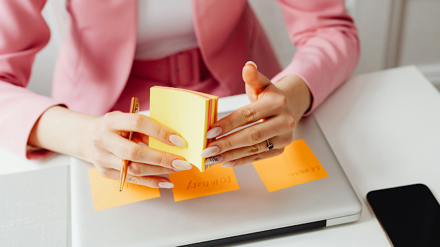 Método Kanban com post-its para organizar tarefas Mãos femininas a organizar notas adesivas coloridas sobre um portátil, representando o uso do método Kanban para planeamento e gestão de tarefas.