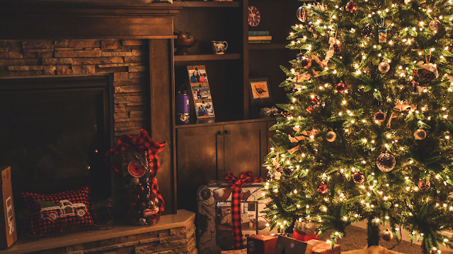 Sala decorada para o Natal com árvore iluminada e presentes Sala acolhedora com árvore de Natal iluminada, presentes com laços vermelhos e lareira decorada, representando o espírito natalício tradicional.