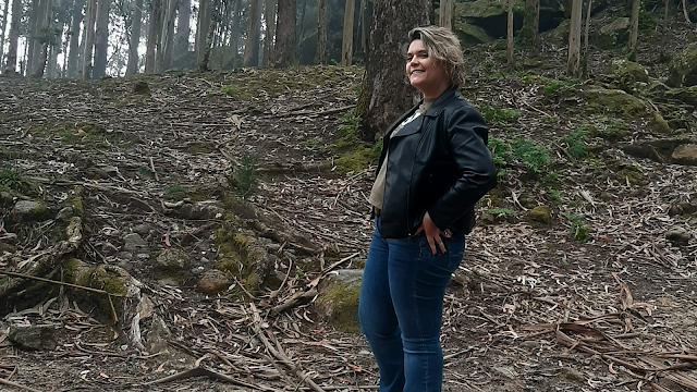 Mulher a sorrir na floresta, representando um momento de reflexão pessoal e crescimento, como na carta ao eu adolescente.
