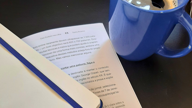 Uma mesa com um caderno, um livro aberto e uma chávena de café, criando uma atmosfera acolhedora e inspiradora para momentos de leitura e reflexão.