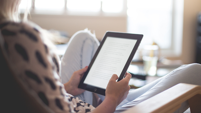 Pessoa a ler um eBook num tablet, sentada confortavelmente em casa, durante o Dia Internacional de Ler um eBook.