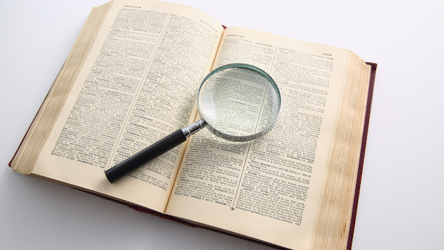 As Palavras Que Nos Fazem Ser Quem Somos Imagem de um dicionário aberto com uma lupa sobre as palavras, representando a importância da língua materna, da leitura e da preservação das línguas.