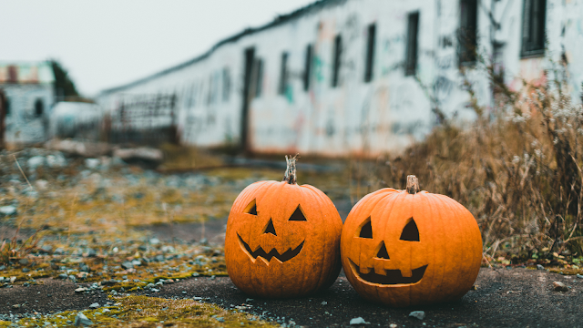 Abóboras Jack-o’-lantern num cenário de Halloween Duas abóboras de Halloween esculpidas com caras sorridentes, colocadas lado a lado num espaço exterior abandonado, criando um ambiente misterioso.
