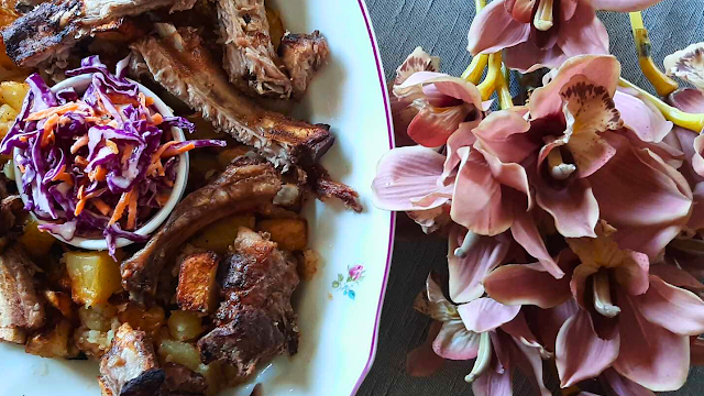 Costelinhas no forno suculentas com batatas Costelinhas de porco assadas no forno com batatas douradas e salada de couve roxa, servidas numa travessa, ao lado de flores decorativas