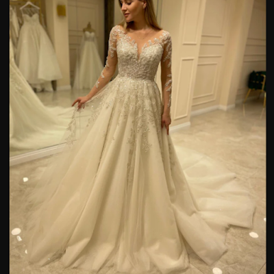 Vestido de noiva romântico com mangas em renda Noiva a experimentar vestido de noiva romântico, com mangas compridas em renda, decote em V e saia fluida em tule, num atelier de noivas