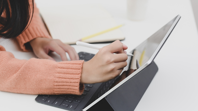 Mão feminina a escrever num tablet com caneta digital, simbolizando tecnologia e organização pessoal.