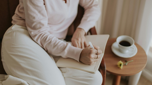 Escrever no diário: um hábito simples do dia-a-dia Pessoa sentada a escrever num caderno, com uma chávena de café ao lado, num momento tranquilo de rotina e reflexão