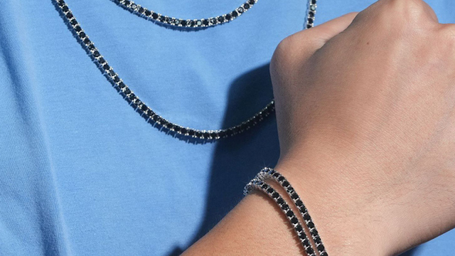Pulseira e colar masculinos em prata com pedras pretas Homem a usar pulseira e colar masculinos prateados com pedras pretas, combinados com t-shirt azul clara