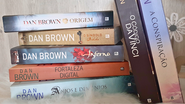 Livros de Dan Brown: uma viagem por mistério e simbologia Pilha de livros de Dan Brown, incluindo Origem, O Código Da Vinci, Inferno, Fortaleza Digital, Anjos e Demónios e O Símbolo Perdido, organizados lado a lado