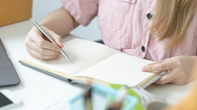 Pessoa a escrever numa agenda em papel Mulher a escrever numa agenda em papel para organizar tarefas e aumentar a produtividade