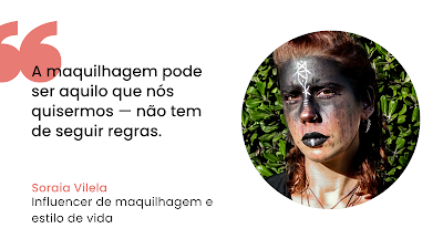 Citação Soraia Vilela: Maquilhagem Sem Regras Grafismo digital de citação sobre fundo branco. À esquerda, aspas grandes em coral precedem o texto preto: "A maquilhagem pode ser aquilo que nós quisermos — não tem de seguir regras." Abaixo, o nome "Soraia Vilela" em coral e a sua ocupação "Influencer de maquilhagem e estilo de vida" em preto. À direita, um retrato fotográfico circular de Soraia Vilela, que tem cabelo ruivo, apresentando uma maquilhagem artística e dramática: o rosto está pintado com pigmento preto mate cobrindo a testa e os olhos, com um símbolo branco geométrico no centro da testa e linhas brancas nos lábios também pintados de preto. O fundo da foto mostra folhagem verde ao ar livre sob luz solar direta.