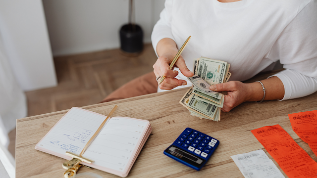 Gestão financeira e cálculo do aumento do IUC em 2026 Pessoa a calcular despesas e a contar dinheiro com uma calculadora e recibos em cima da mesa, representando o impacto do aumento do IUC em 2026 nos orçamentos familiares.