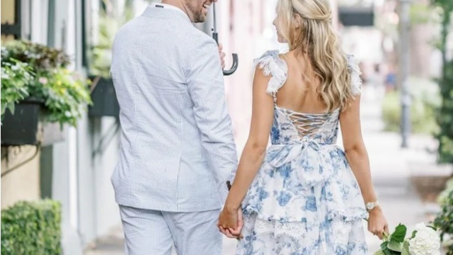 Coordinated Garden Wedding Attire: Floral Midi Dress and Seersucker Suit A couple walks hand-in-hand outdoors, showcasing elegant garden wedding fashion. The woman is wearing a blue and white floral dress with lace trim and a corset-style back. The man is wearing a light blue seersucker summer suit. The aesthetic is romantic, classic, and perfect for an outdoor ceremony.