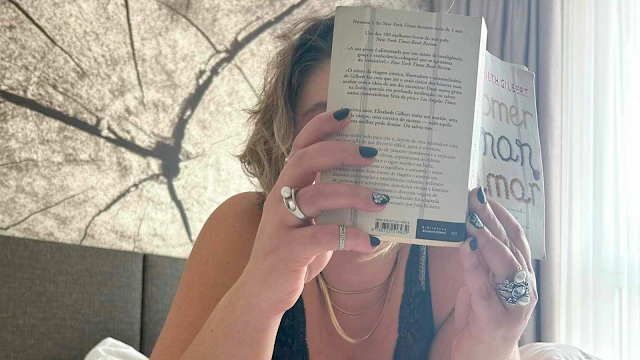 eresa Isabel Silva relaxando e lendo um livro num quarto de hotel, rodeada de conforto e tranquilidade, aproveitando um momento de introspecção e descanso