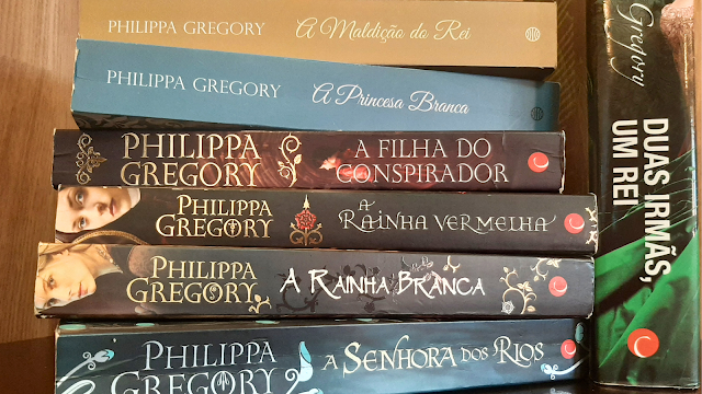 Livros das Sagas Tudor e Guerra dos Primos em Português Pilha vertical de livros da autora Philippa Gregory com as lombadas visíveis. De cima para baixo: 'A Maldição do Rei', 'A Princesa Branca', 'A Filha do Conspirador', 'A Rainha Vermelha', 'A Rainha Branca' e 'A Senhora dos Rios'. À direita, destaca-se a lombada vertical do livro 'Duas Irmãs, Um Rei'.